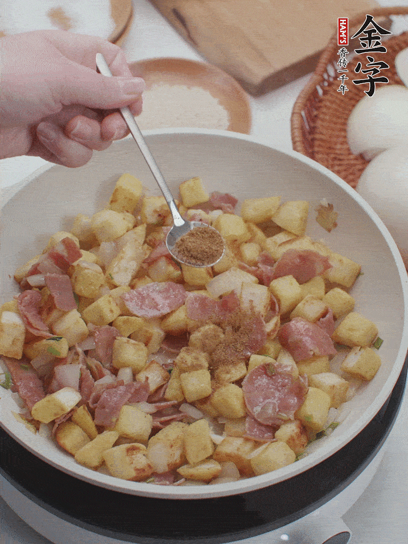 起鍋少油，煸香洋蔥丁、蔥白，加入金字培根火腿翻炒幾下，再加入饅頭丁、1小勺孜然粉、少許鹽翻炒均勻并鋪平。